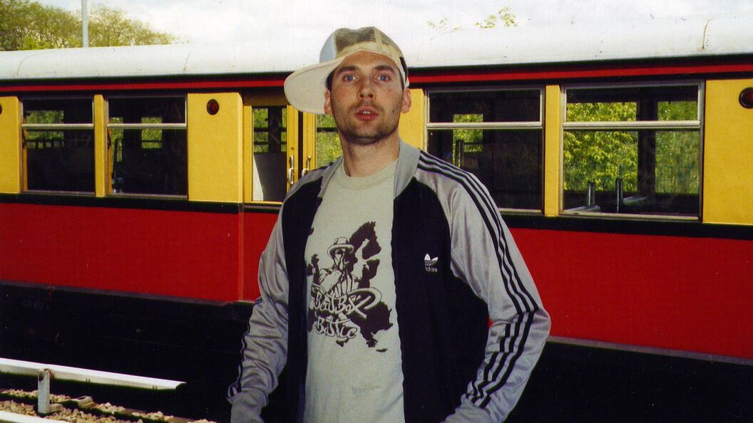 Bee Low the Graffiti pioneer is standing in a Berlin train yard with a classic BR477 S-Bahn in the background